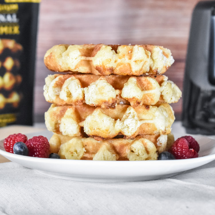 A stack of Liège waffles on a plate with fresh berries and a drizzle of syrup.